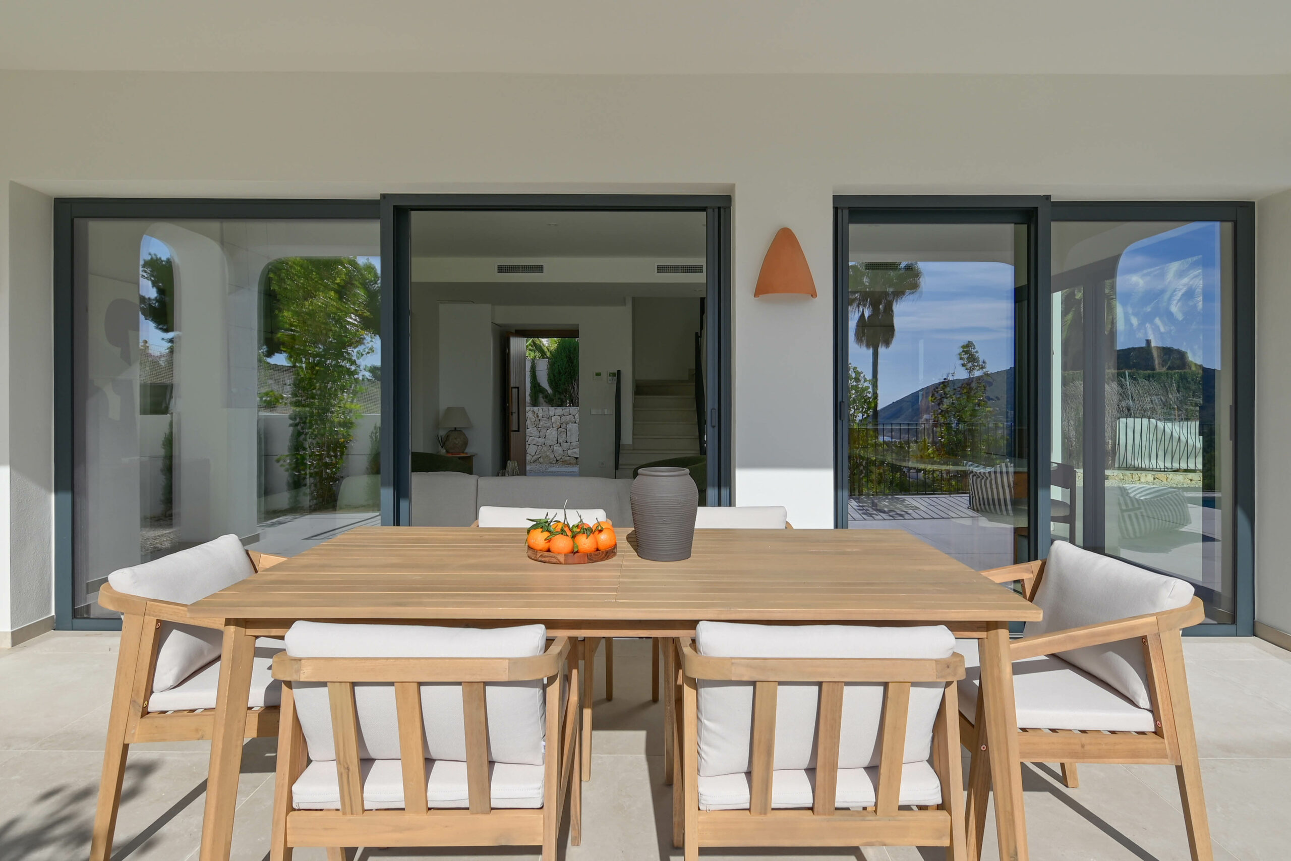 outdoor-living Modern Mediterranean villa terrace with wooden outdoor dining furniture and large sliding glass doors opening to the interior.